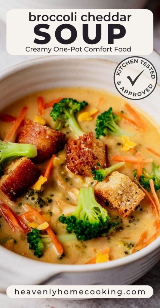 Close-up of creamy broccoli cheddar soup topped with broccoli florets, shredded carrots, cheddar, and golden croutons. This is a Pinterest pin for a Heavenly Home Cooking recipe.