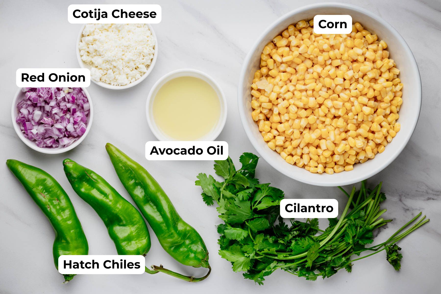 Labeled Hatch chile corn salad ingredients, including corn, Hatch chiles, Cotija cheese, red onion, cilantro, and avocado oil.