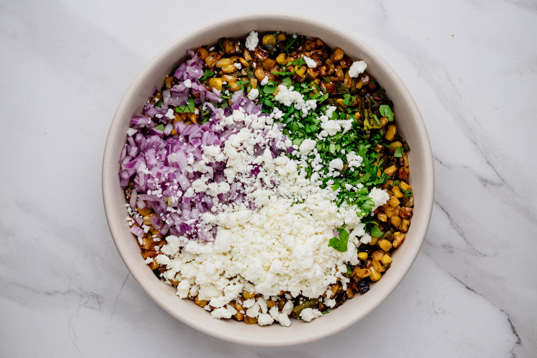 Charred corn and Hatch chiles topped with diced red onion, Cotija cheese, and chopped cilantro in a bowl.