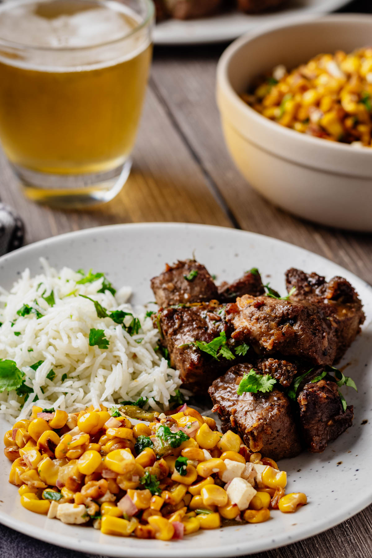Hatch chile steak bites served with cilantro lime rice and corn salad, with a glass of beer in the background.