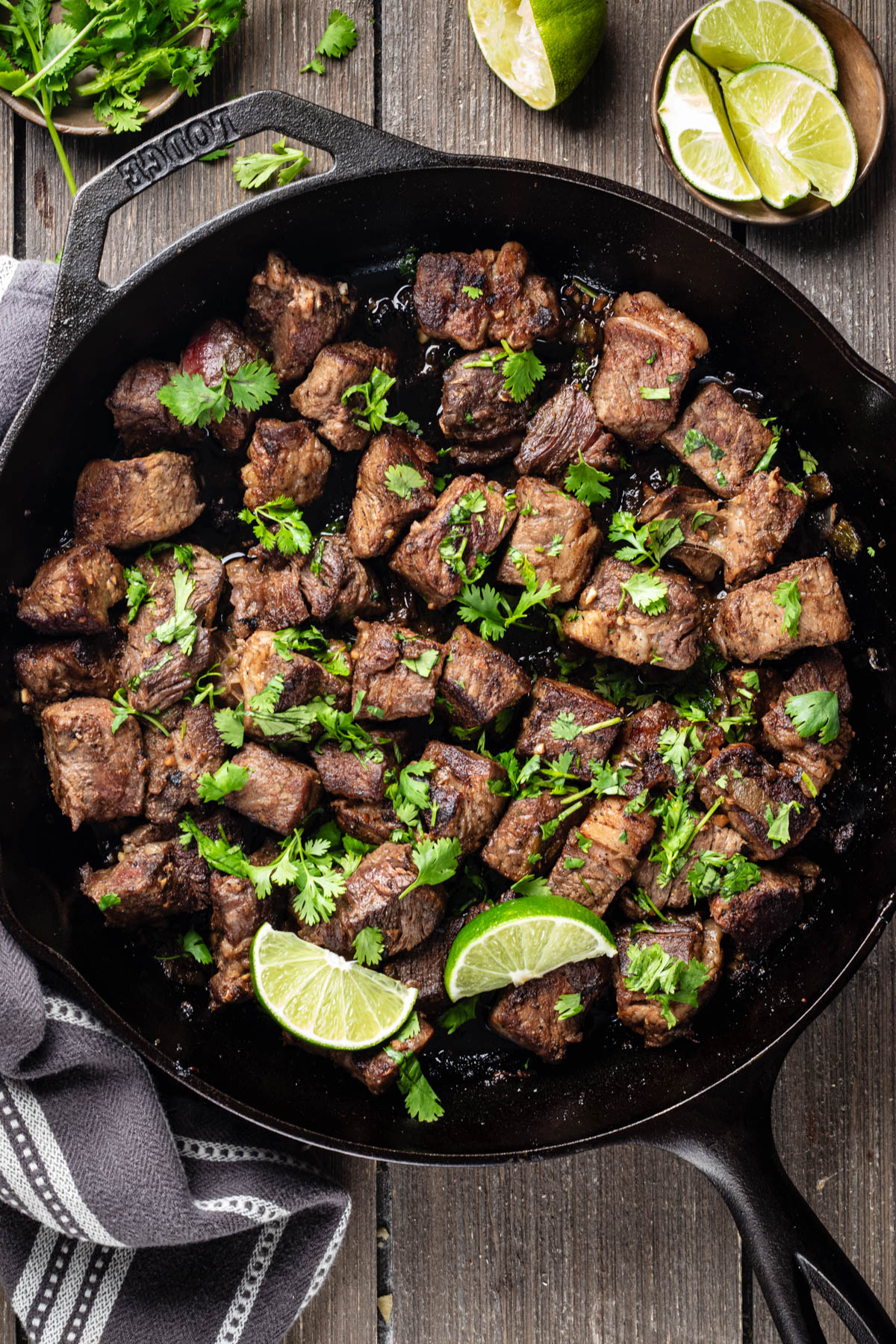 Hatch chile steak bites with browned edges, cilantro, and lime wedges in a cast-iron skillet.