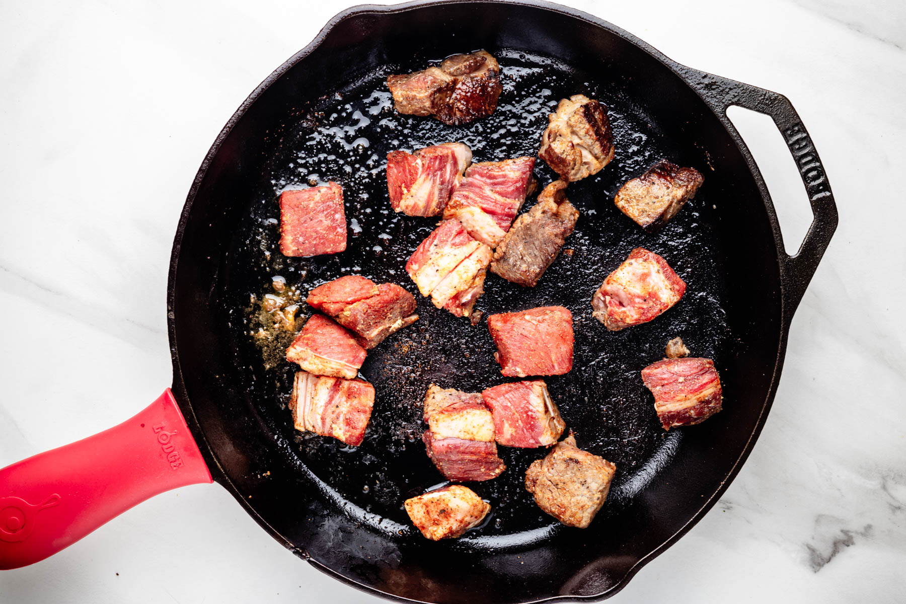 Seasoned steak cubes developing a brown crust in a hot cast-iron skillet.