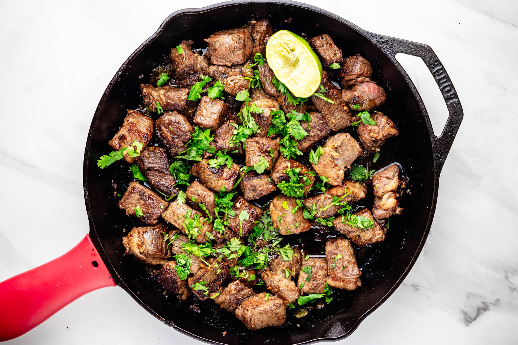 Hatch chile steak bites finished with chopped cilantro and fresh lime in a cast-iron skillet.