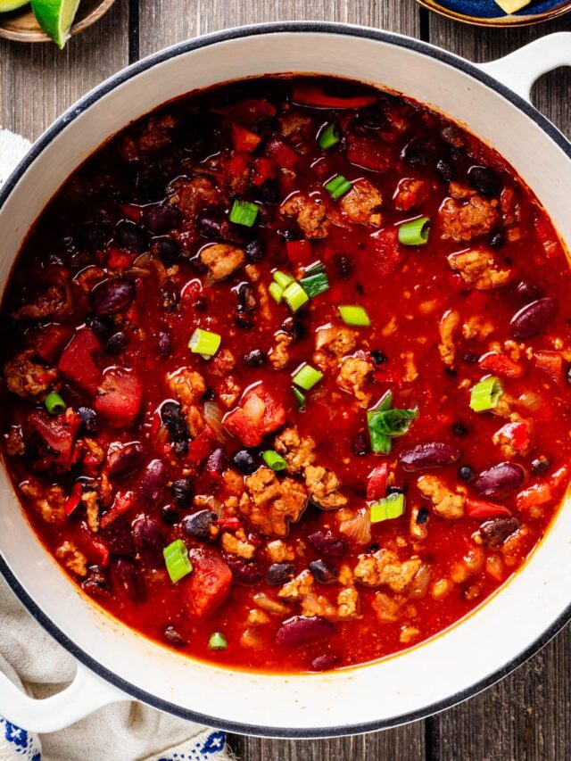 Overhead view of healthy turkey chili with ground turkey, black beans, kidney beans, tomatoes, and red bell pepper in a white Dutch oven.