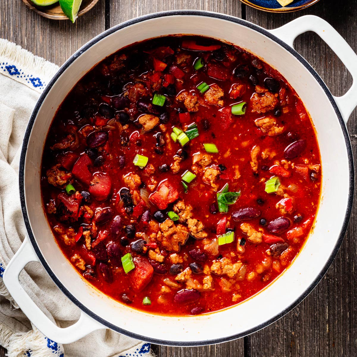 Overhead view of healthy turkey chili with ground turkey, black beans, kidney beans, tomatoes, and red bell pepper in a white Dutch oven.