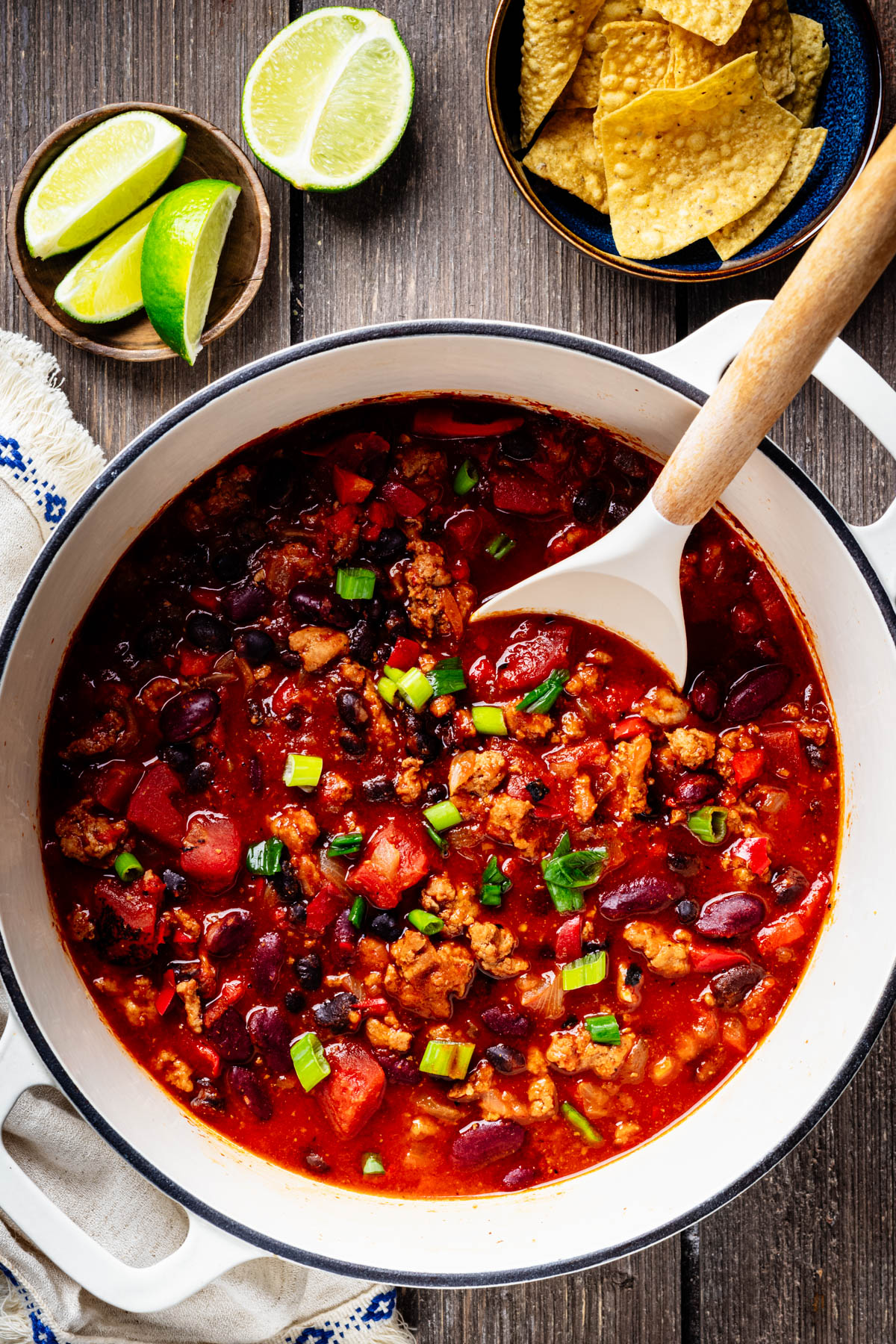 Healthy turkey chili with ground turkey, beans, tomatoes, and bell pepper being ladled from a white Dutch oven.