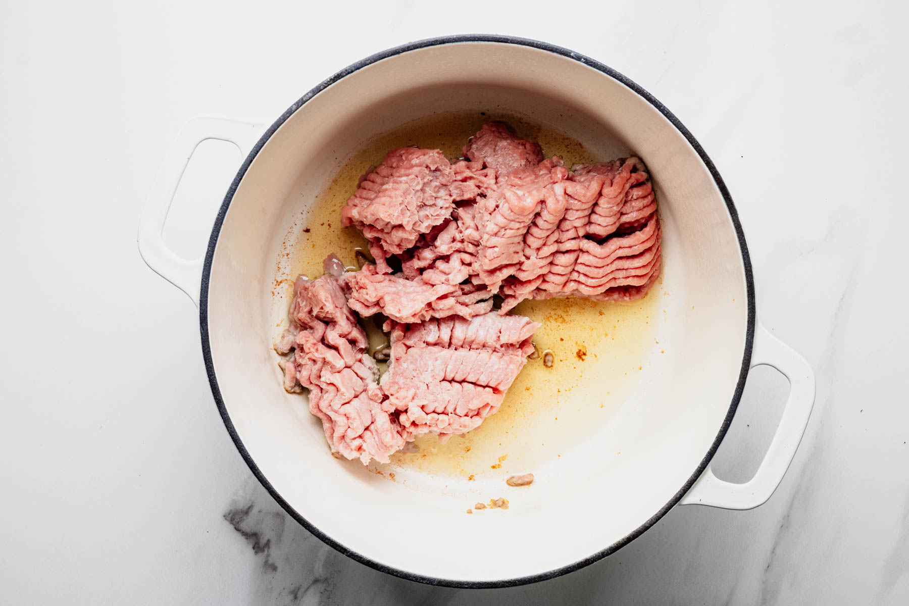 Raw ground turkey cooking in olive oil in a white Dutch oven.