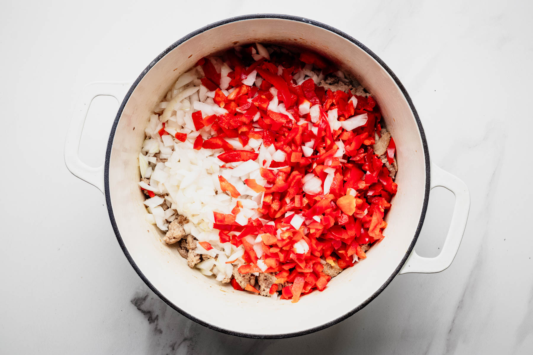 Diced onion and red bell pepper added to browned ground turkey in a Dutch oven.