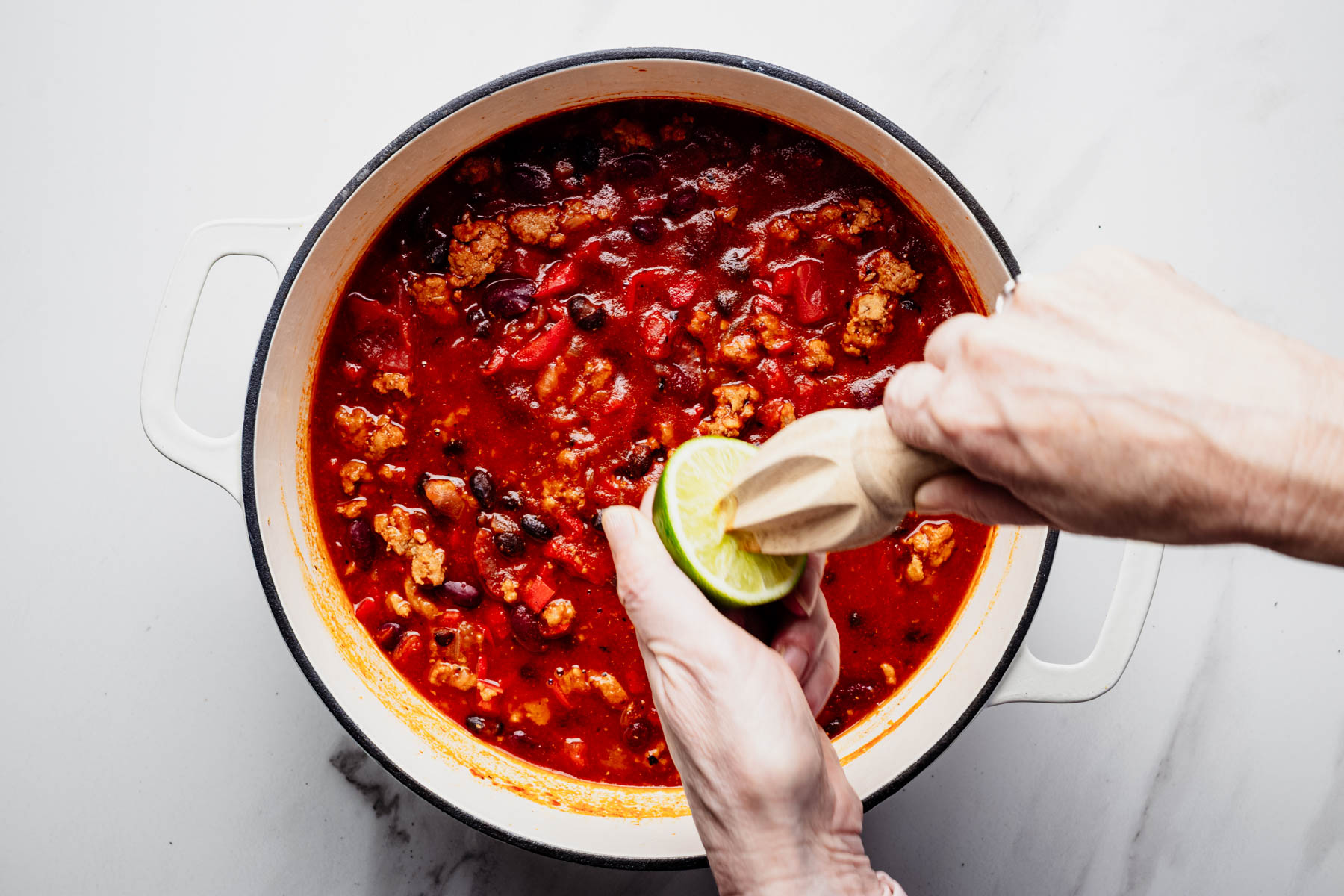 Fresh lime juice being squeezed into a Dutch oven of healthy turkey chili.