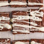 Close-up of mummy brownies decorated with white chocolate drizzle and candy eyes on parchment paper.