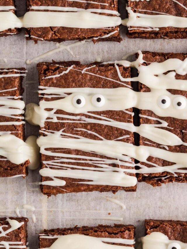 Close-up of mummy brownies decorated with white chocolate drizzle and candy eyes on parchment paper.