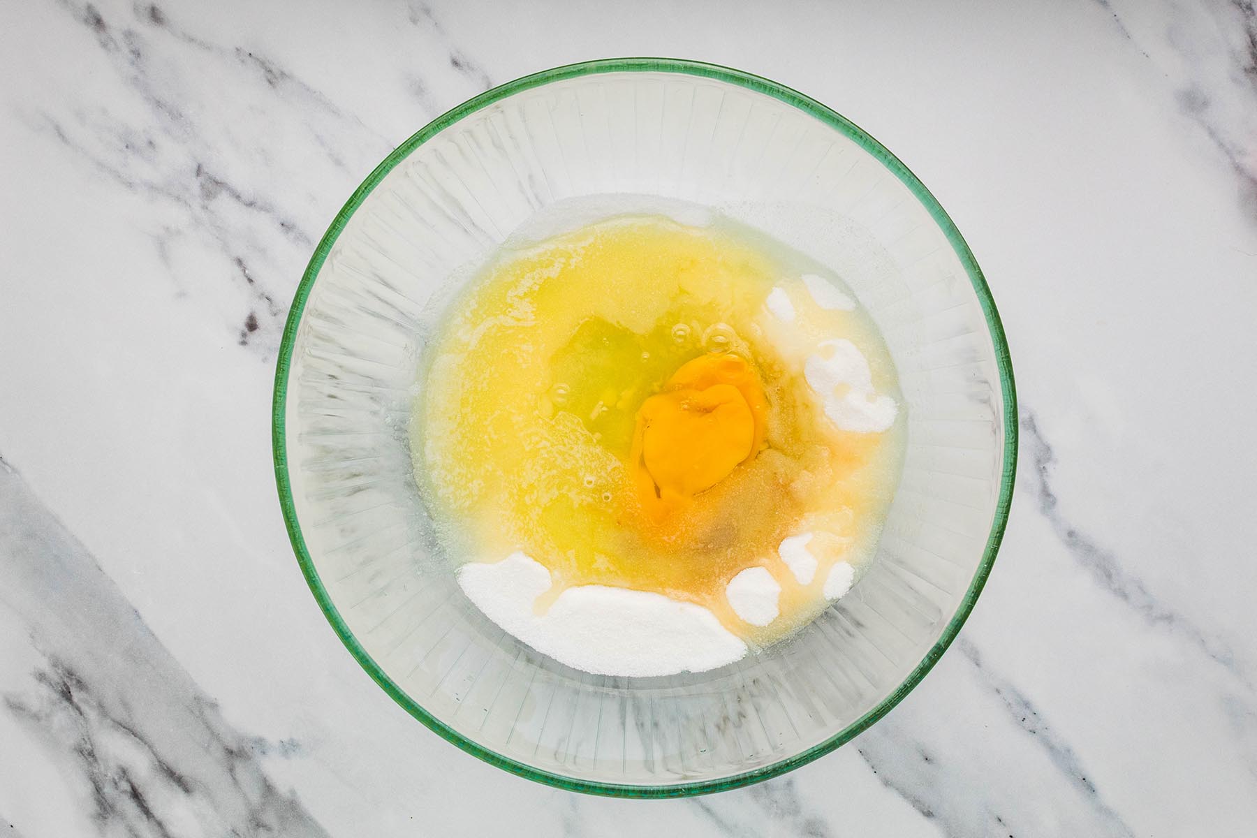 Granulated sugar, melted butter, egg, egg yolk, and vanilla in a glass mixing bowl.
