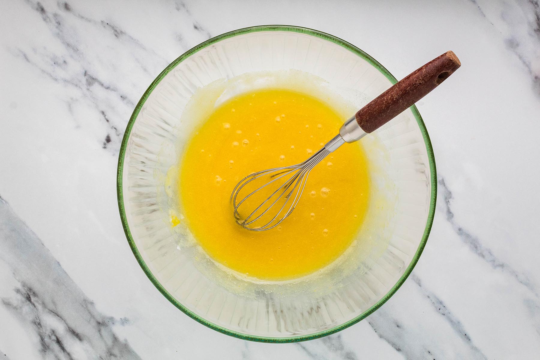 Whisked sugar, butter, eggs, and vanilla mixture in a glass bowl.