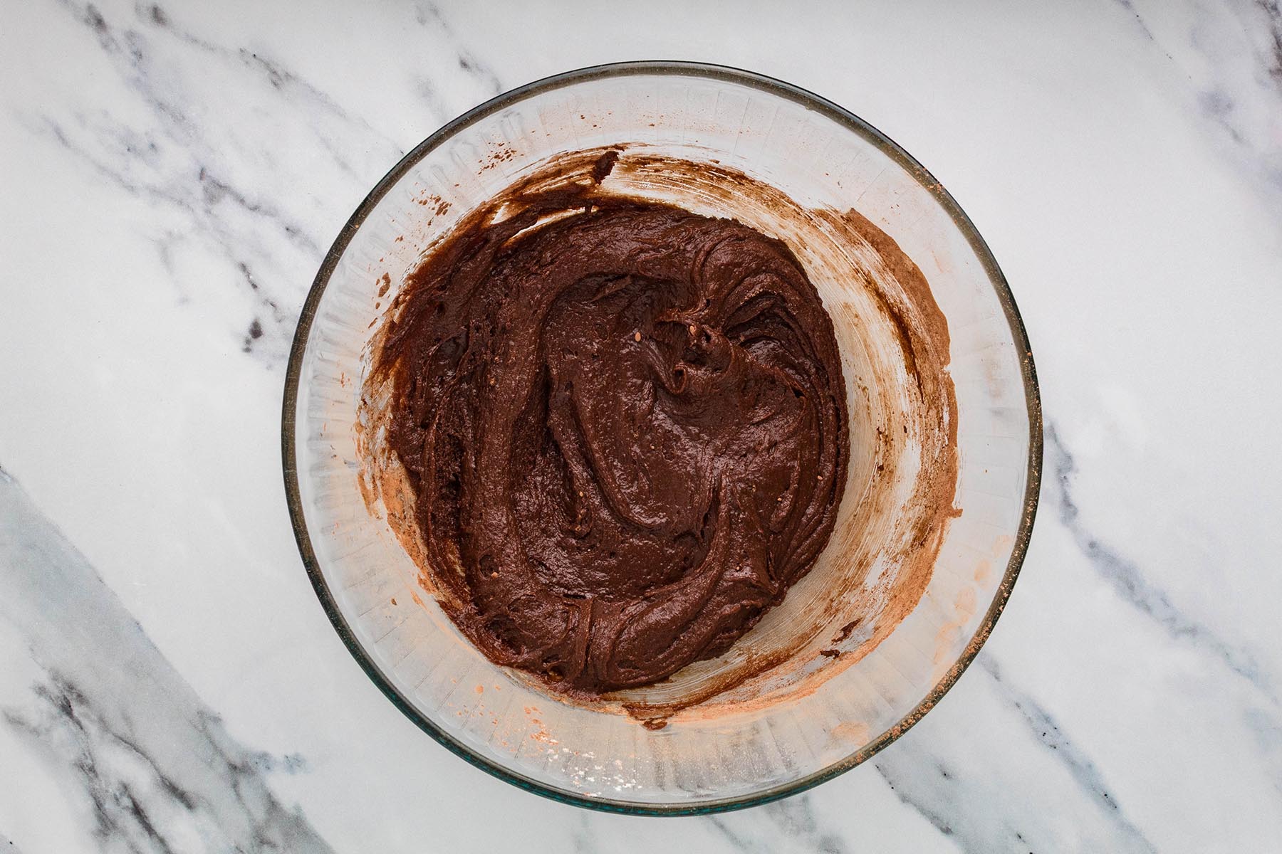 Thick chocolate brownie batter mixed in a glass bowl.