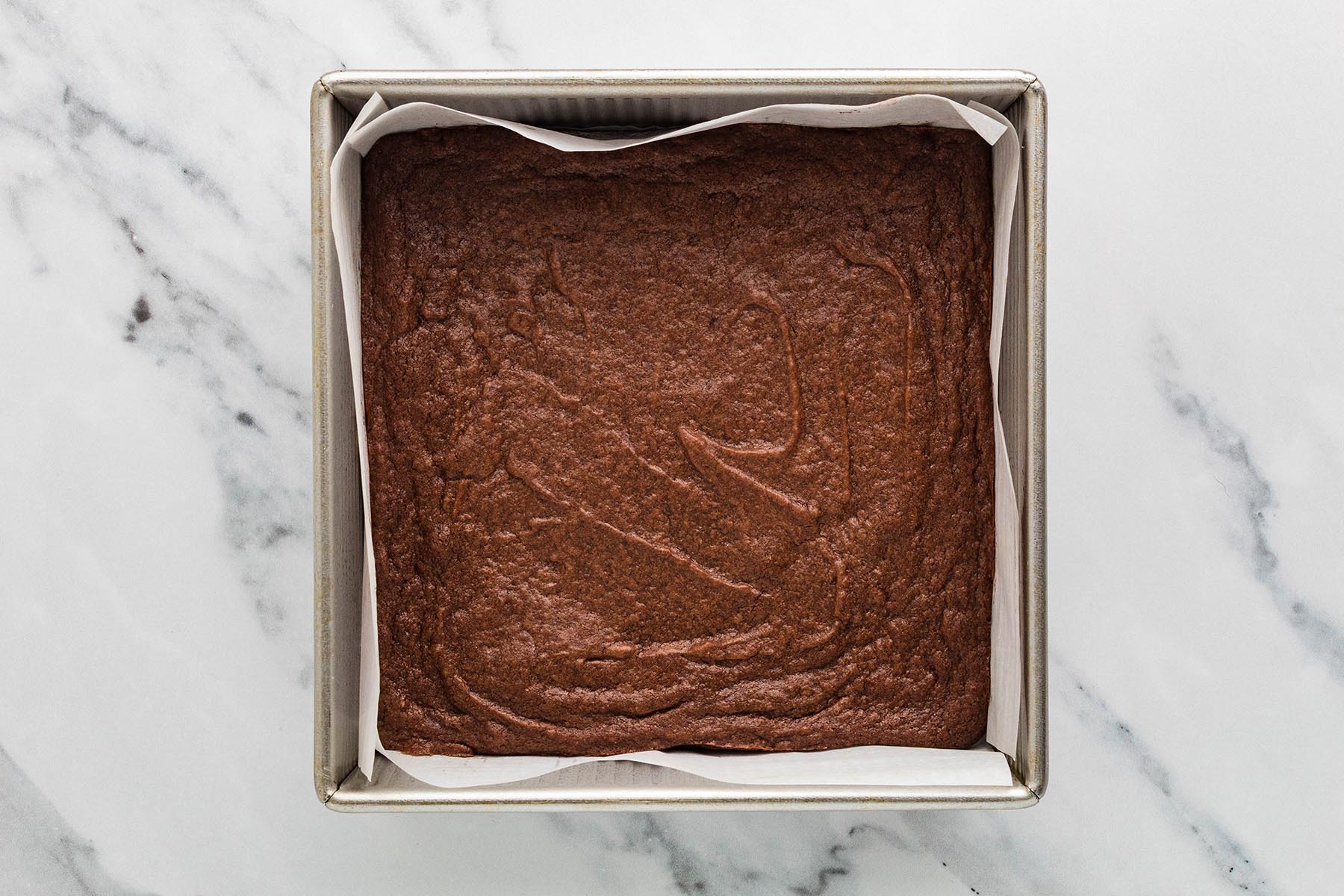 Baked chocolate brownies cooling in a parchment-lined square metal pan.