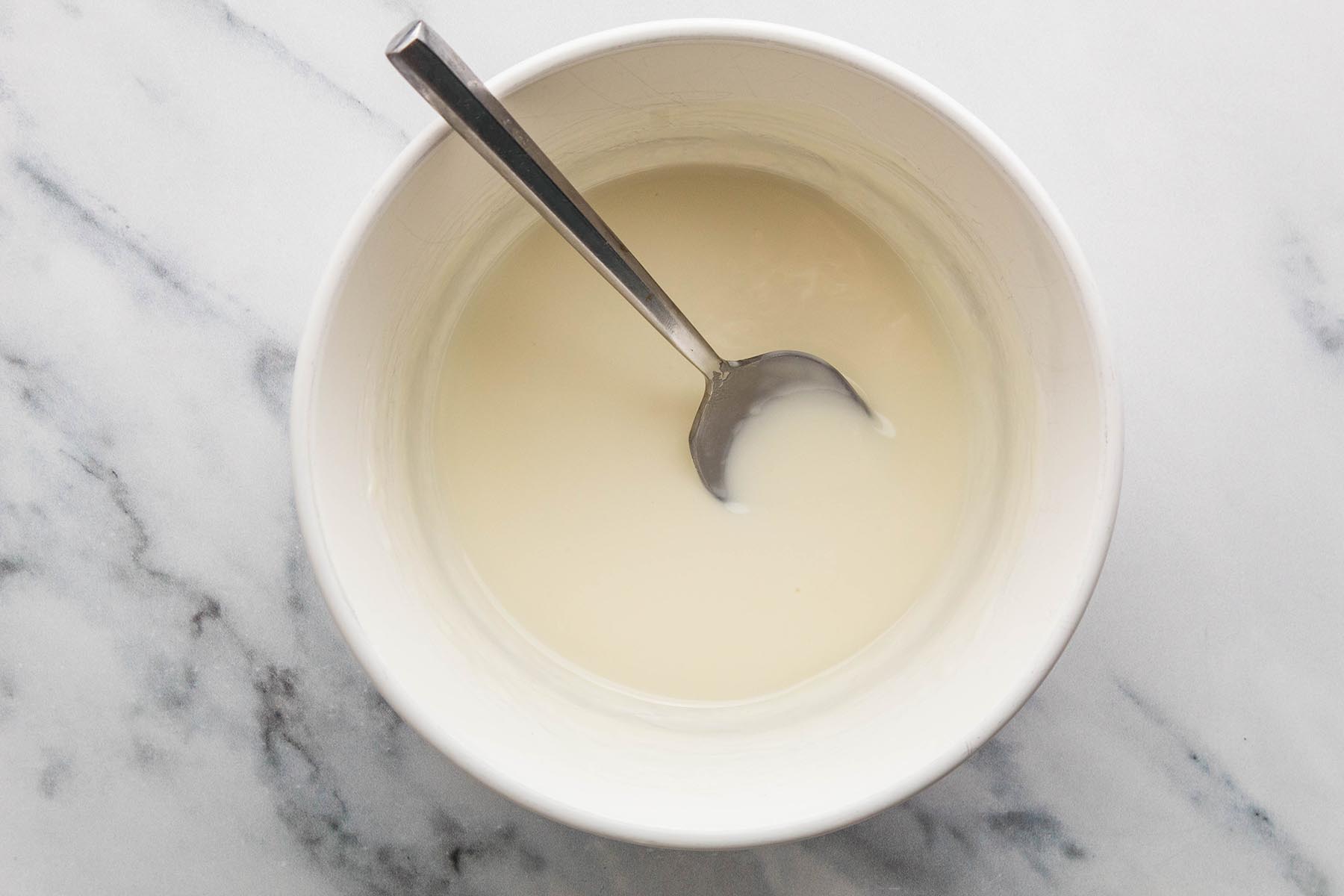 Smooth melted white chocolate and coconut oil in a bowl with a spoon.