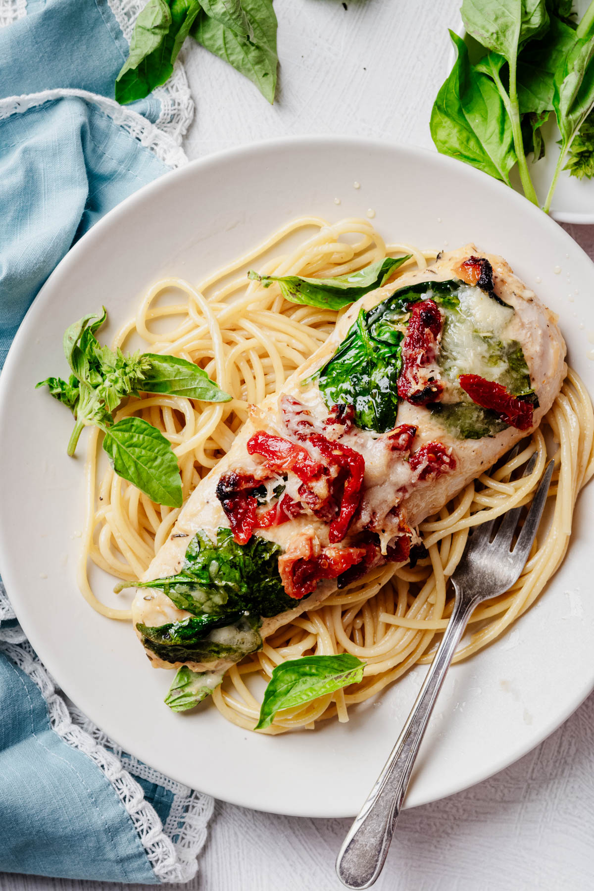 Sheet pan Tuscan chicken topped with spinach, sun-dried tomatoes, melted Parmesan, and fresh basil, served over spaghetti on a white plate.