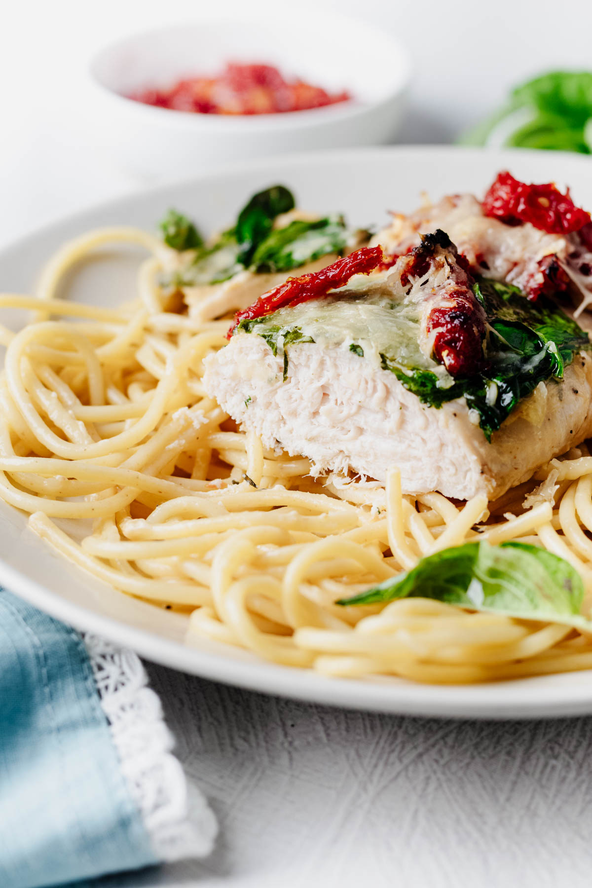Close-up of sliced Tuscan chicken topped with spinach, sun-dried tomatoes, and melted Parmesan, served over spaghetti.