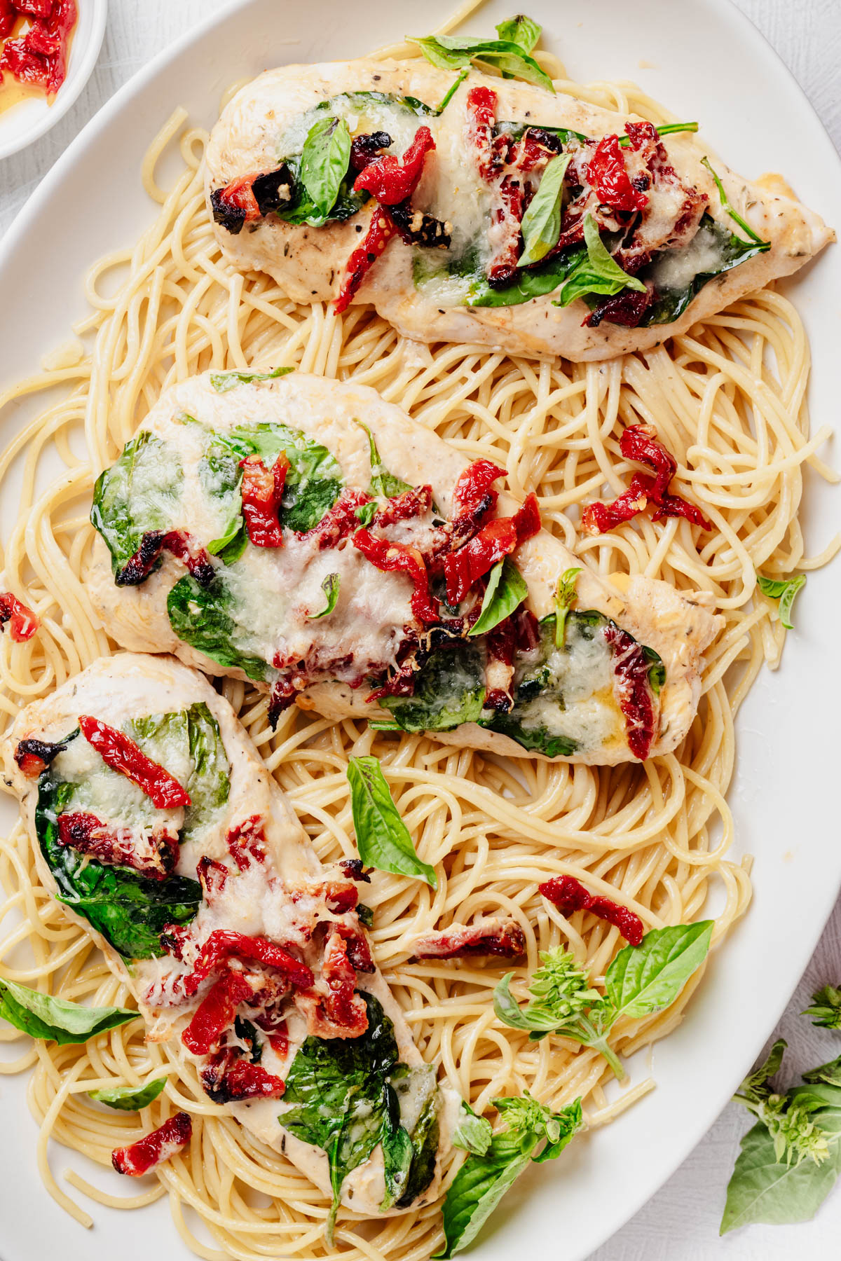 Overhead close-up of Tuscan chicken cutlets topped with spinach, sun-dried tomatoes, melted Parmesan, and fresh basil over spaghetti.