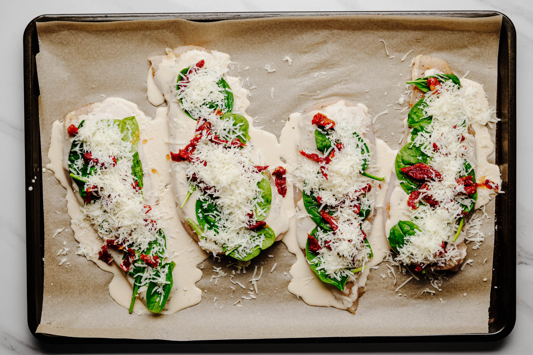 Seasoned chicken cutlets topped with Alfredo sauce, fresh spinach, chopped sun-dried tomatoes, and grated Parmesan before baking.