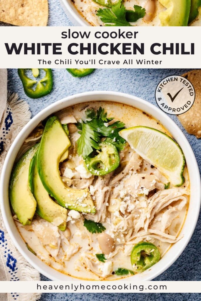 Vertical Pinterest pin for slow cooker white chicken chili featuring a bowl of creamy white chicken chili topped with avocado slices, shredded chicken, white beans, jalapeños, cilantro, crumbled cheese, and a lime wedge. The text overlay reads "Slow Cooker White Chicken Chili" with the subtitle "The Chili You'll Crave All Winter," and includes a Kitchen Tested & Approved badge and the Heavenly Home Cooking logo.